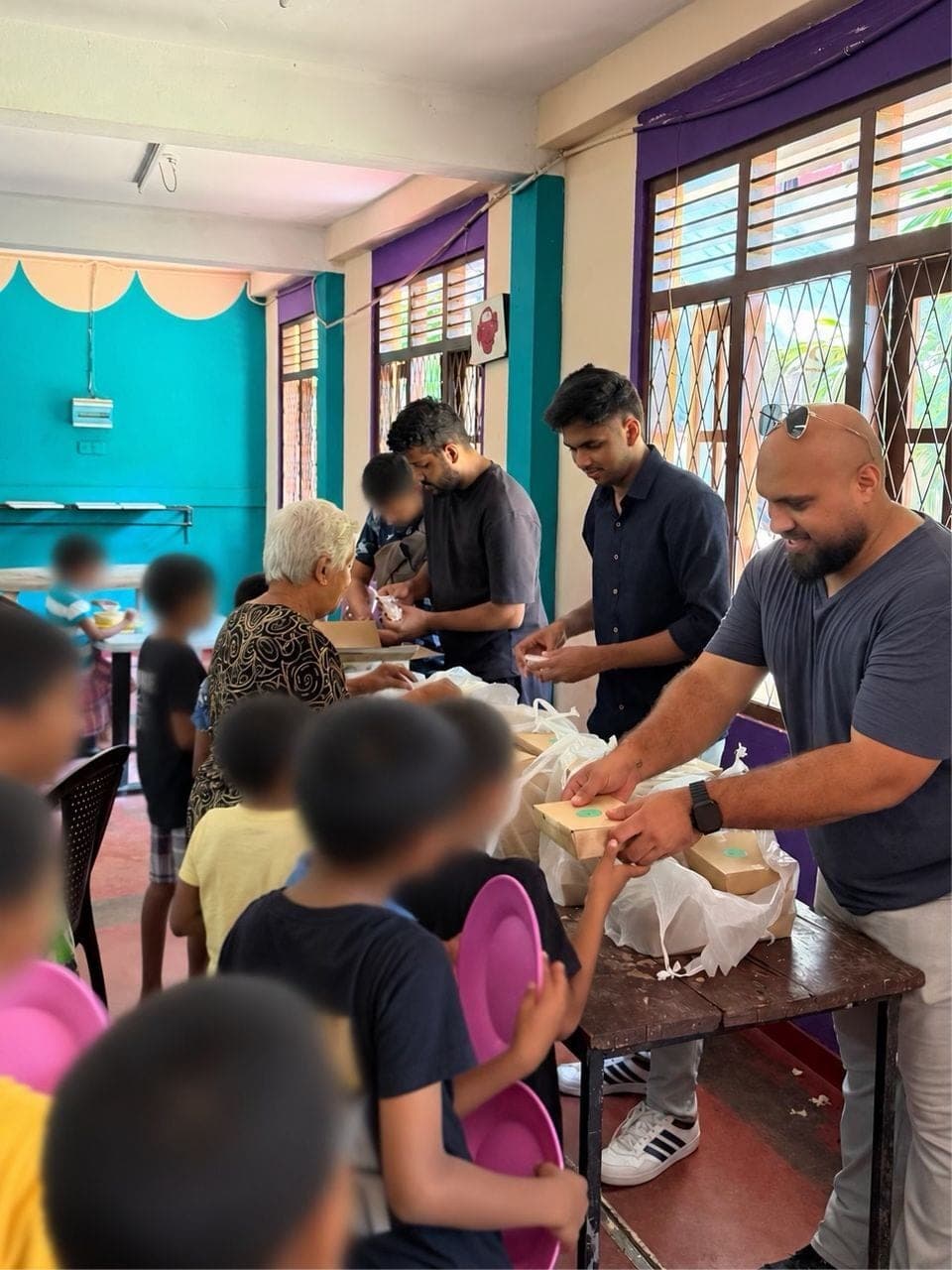 Coderra team members handing out boxed lunches to a line of children holding plates, children's faces blurred for privacy.
