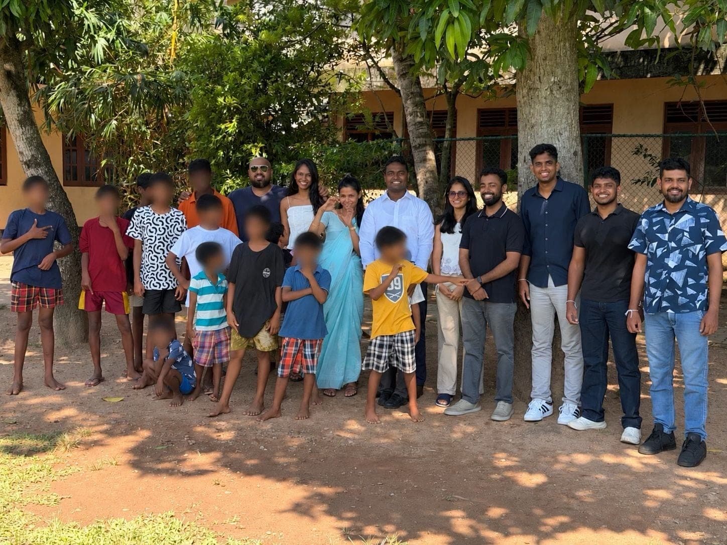 The Coderra team standing with children from Vajira Sri Children's Development Centre under the trees in the centre's grounds, children's faces blurred for privacy.